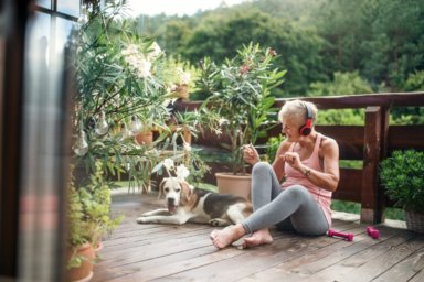 Frau sitzt auf einer Terrasse neben einem Hund, hört über Kopfhörer Musik und tanzt