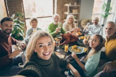 Eine Frau macht ein Selfie bei einem Familienessen mit jung und alt.