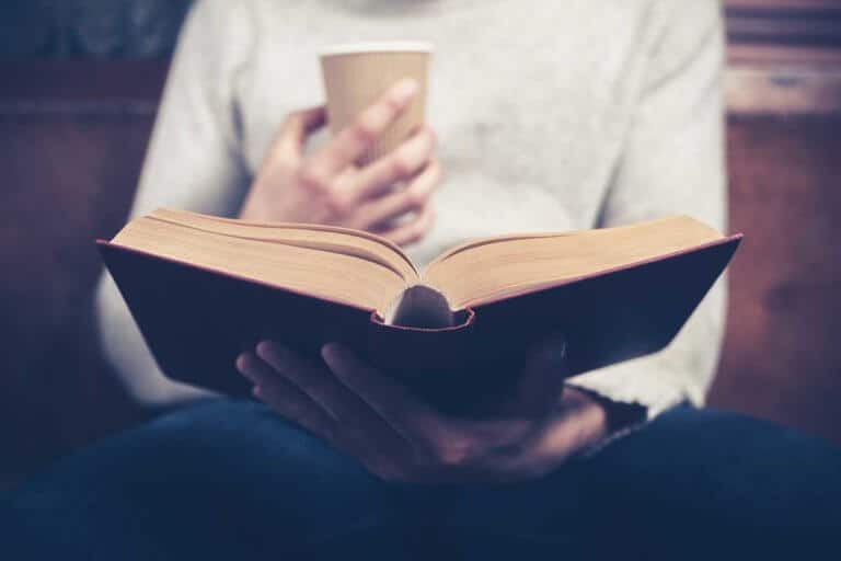 Junger Mann liest ein Buch und trinkt Kaffee.